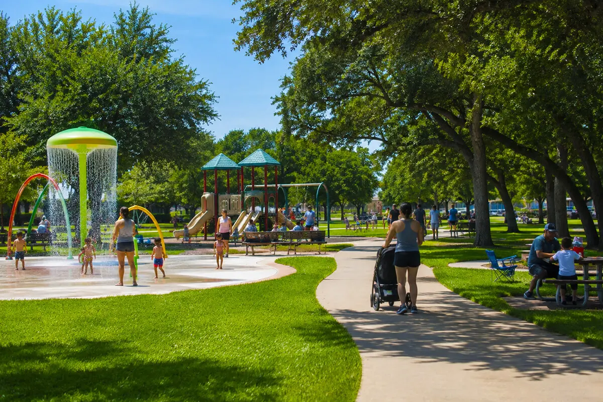 Families enjoying a community park with a splash pad, playground, and walking trail