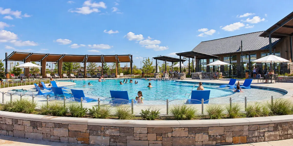 Resort-style community pool with lounge chairs, shaded seating, and clubhouse amenities in Fulshear, Texas.